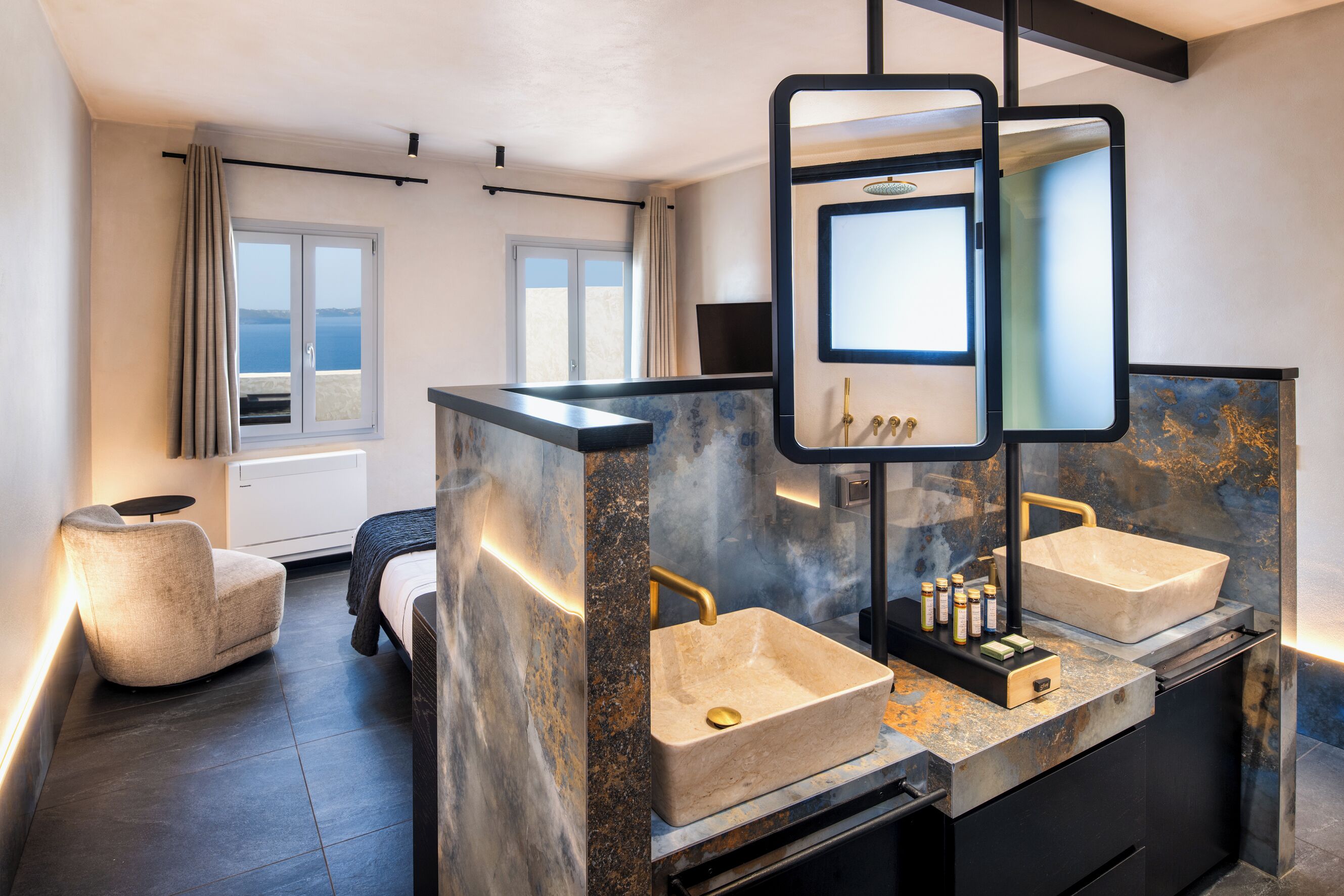A modern bathroom with two sinks, a large mirror, and a view of the sea through the window.