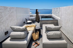A rooftop terrace with a sofa, a small table, a chair, a hot tub, and a view of the sea. - Imerti Suites (Santorini)