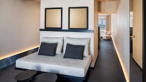 Quarto de hotel moderno com uma cama grande, duas mesinhas de cabeceira e vista para o corredor.