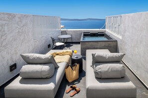 A rooftop terrace with two sofas, a small table, a chair, a hot tub, and a view of the sea. - Imerti Suites (Santorini)