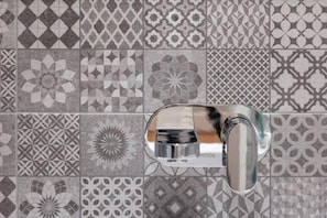 A bathroom with a modern chrome faucet and a tiled wall featuring various geometric and floral patterns.