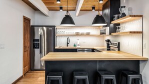 Una cocina moderna con una isla central, electrodomésticos de acero inoxidable, detalles de madera e iluminación colgante.