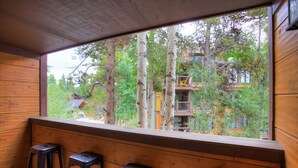 Interior de madera con un amplio ventanal que da a un área boscosa y un edificio con balcones.