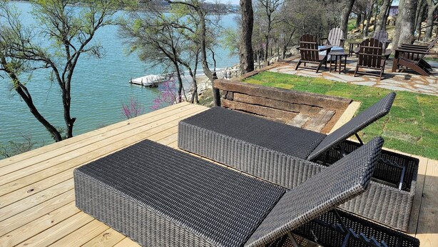 Um terraço com mobiliário de vime, com vista para um lago, cercado por árvores.
