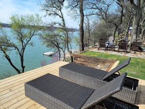 Een terras met rieten meubilair met uitzicht op een meer, omringd door bomen.