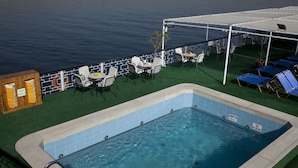 A pool area with a view of a lake, surrounded by lounge chairs and a covered seating area. - JAZ Helio Nile Cruise - Every Monday from Luxor for 07 & 04 Nights - Every Friday From Aswan for 03 Nights (Luxor)
