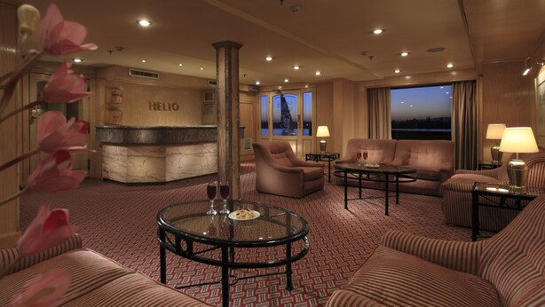 A hotel lobby with a reception desk, sofas, a coffee table, and a view of the cityscape at dusk. - JAZ Helio Nile Cruise - Every Monday from Luxor for 07 & 04 Nights - Every Friday From Aswan for 03 Nights (Luxor)