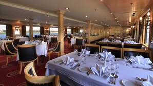 A spacious dining area with multiple tables set for service, large windows offering a view of the water, and a high ceiling with recessed lighting. - JAZ Helio Nile Cruise - Every Monday from Luxor for 07 & 04 Nights - Every Friday From Aswan for 03 Nights (Luxor)