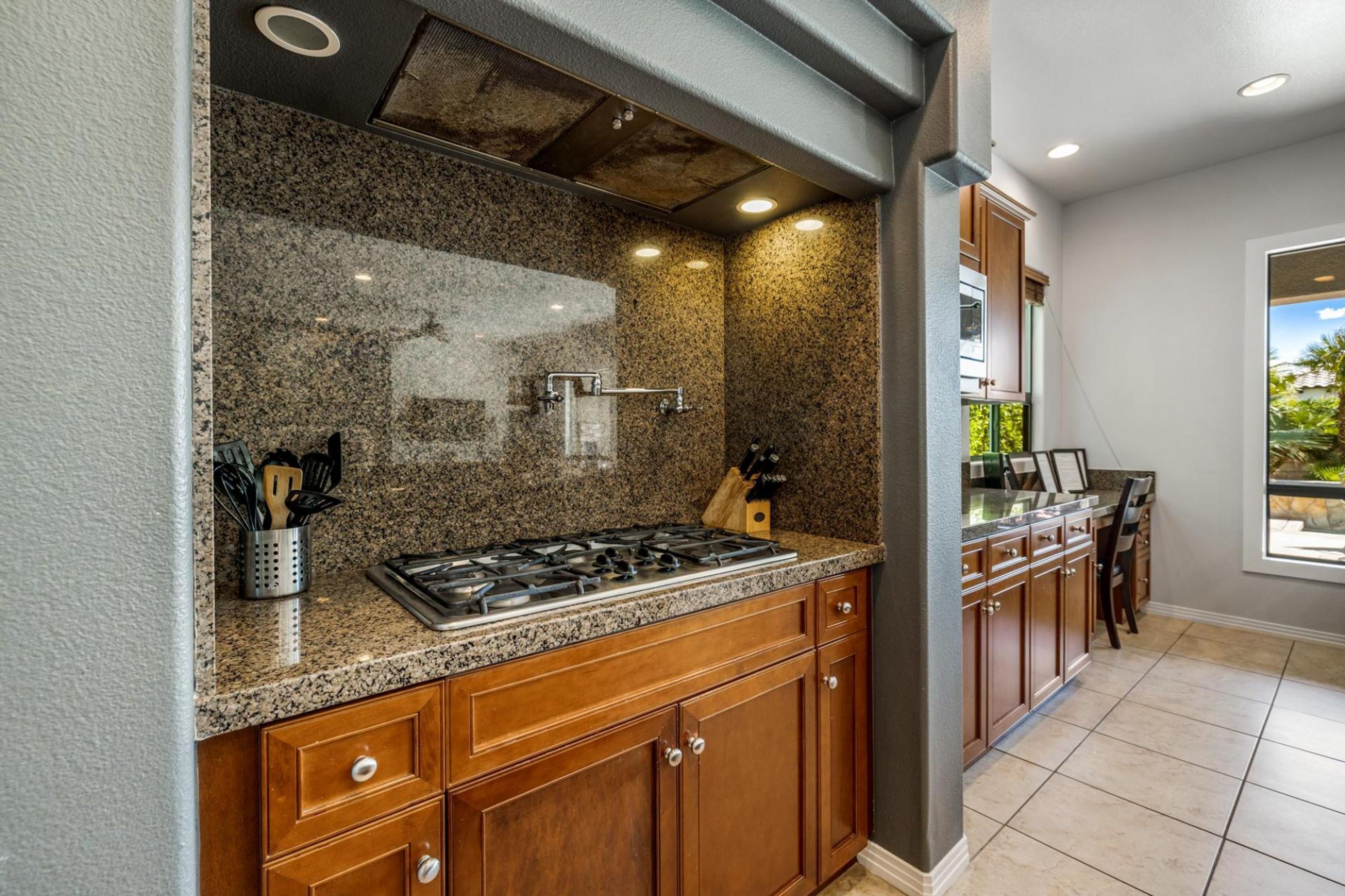 A kitchen with granite countertops, wooden cabinets, a gas stove, and a window providing a view of the outdoors.