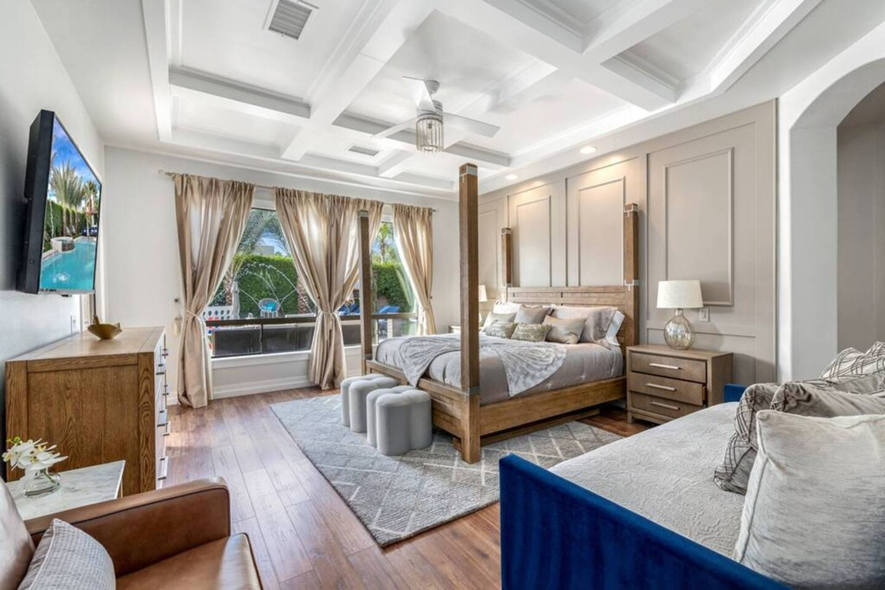 A bedroom with a large bed, a TV, a wooden dresser, and a window with curtains.
