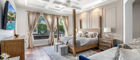 A bedroom with a large bed, a TV, a wooden dresser, and a window with curtains.