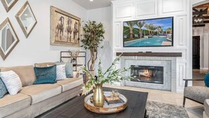 Una sala de estar con chimenea, televisor montado y un sofá con almohadones decorativos.