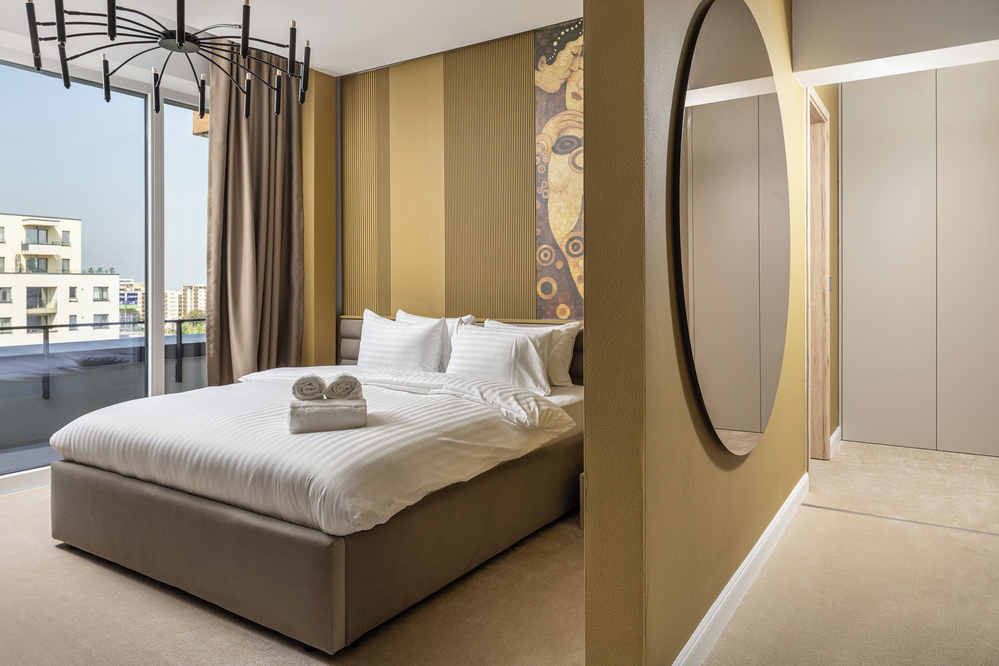 A modern hotel room with a large bed, a view of the city, and a unique wall design.