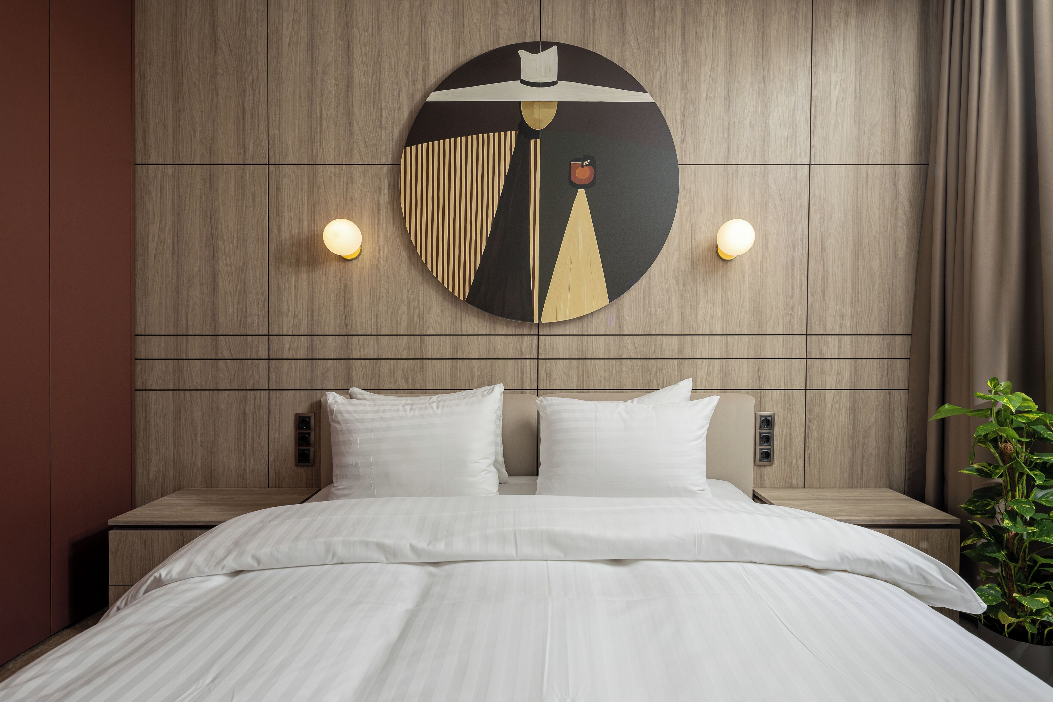 A modern hotel room with a large bed, two bedside tables, and a wall-mounted artwork.