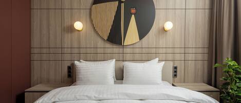 A modern hotel room with a large bed, two bedside tables, and a wall-mounted artwork.