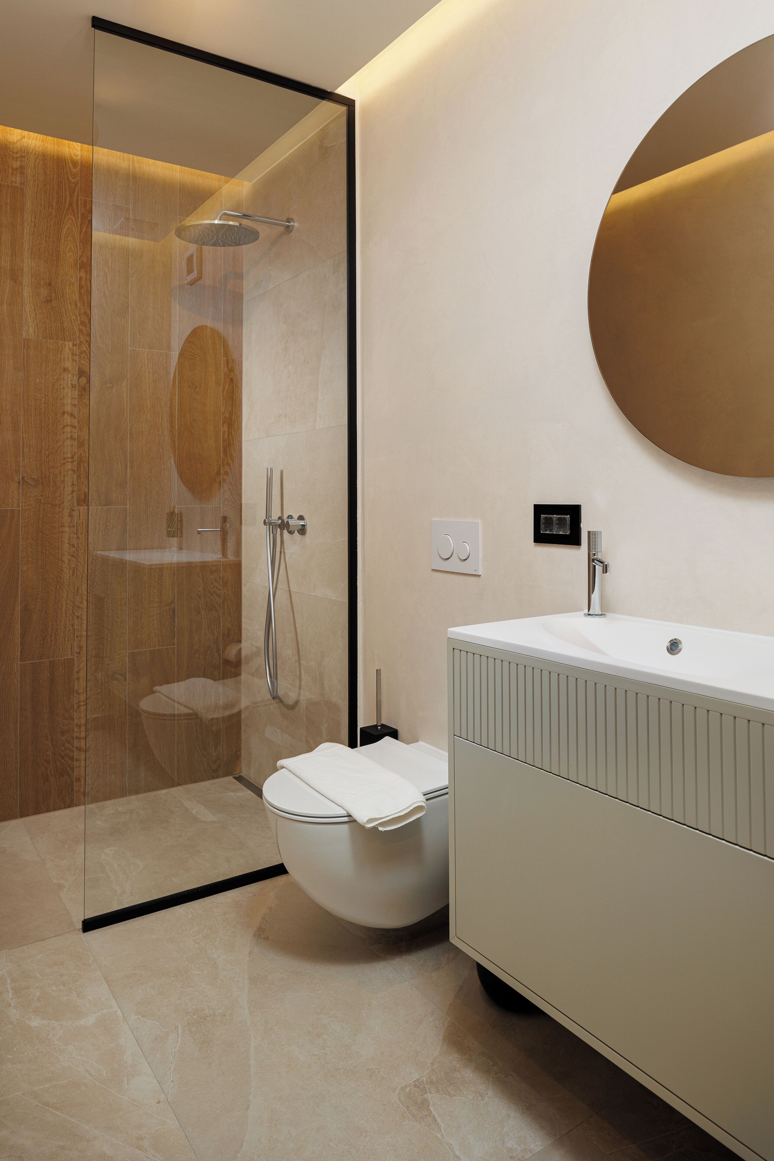 A modern bathroom with a glass-enclosed shower, a white toilet, and a vanity with a round mirror.