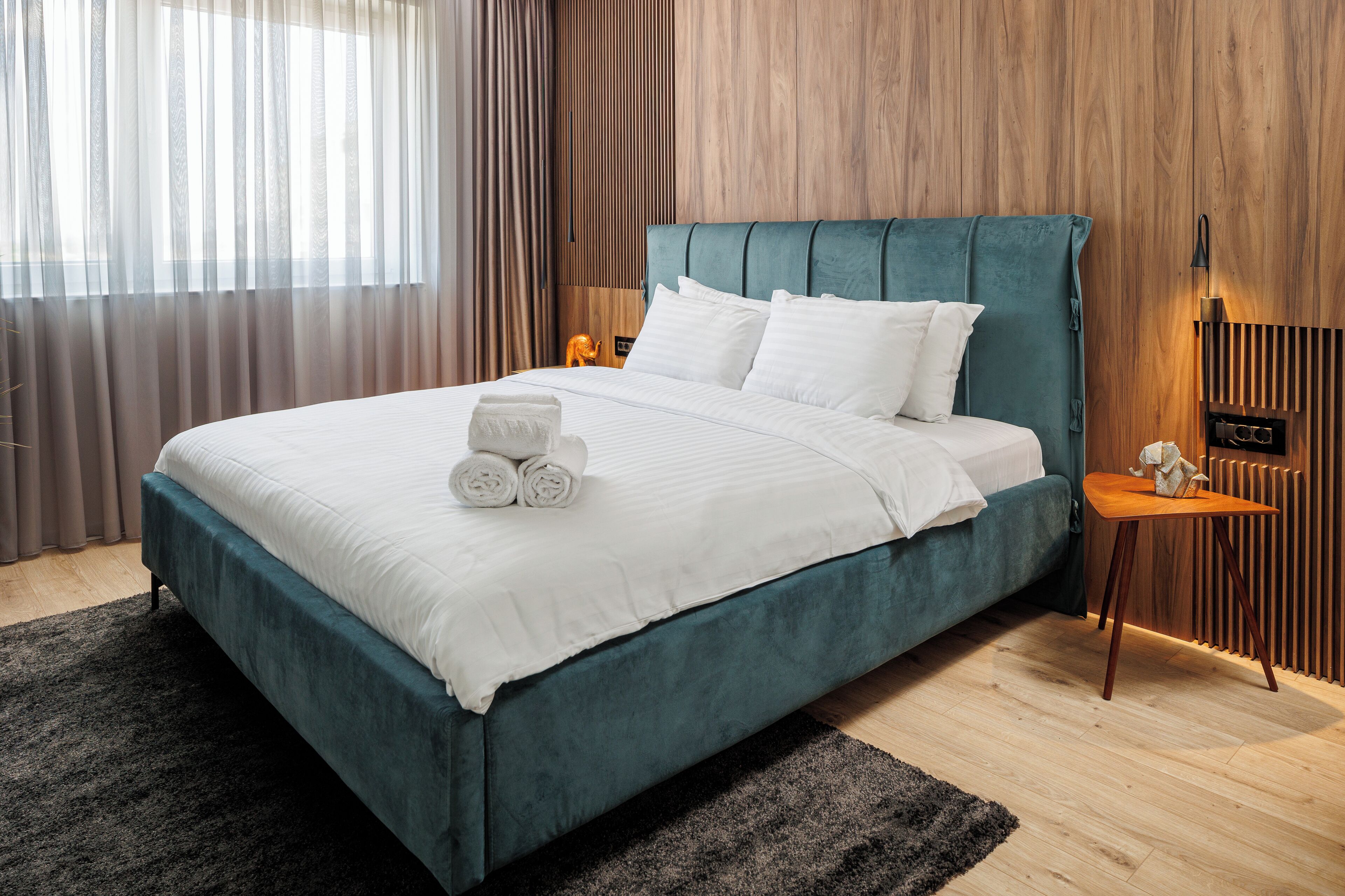 Une chambre moderne avec un lit de couleur turquoise, une literie blanche et une tête de lit en bois.