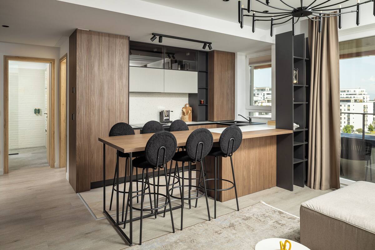 A modern kitchen with a wooden island, black bar stools, and a view of the city through large windows.