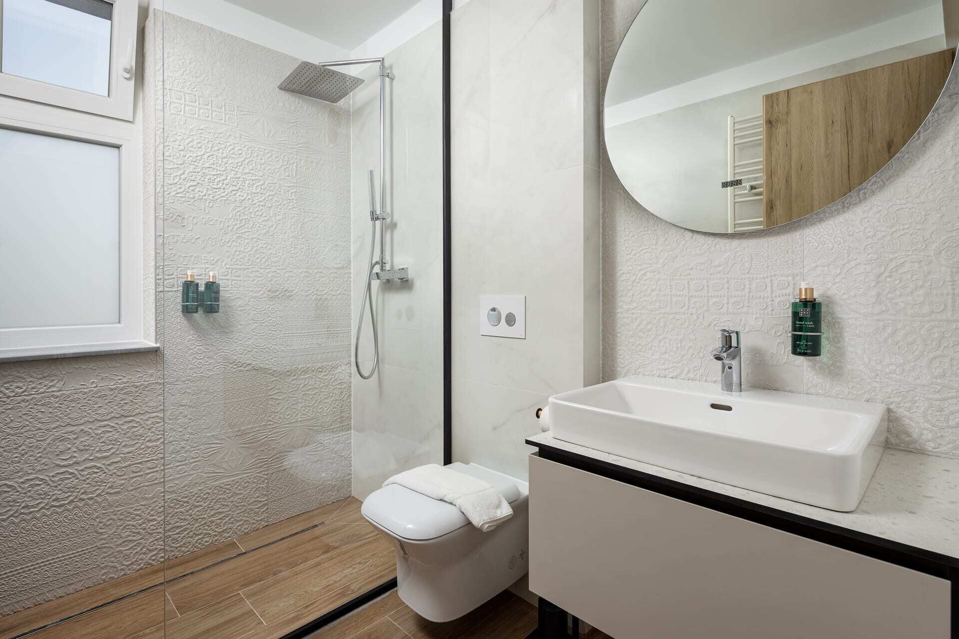 A modern bathroom with a walk-in shower, a toilet, a sink, and a mirror.