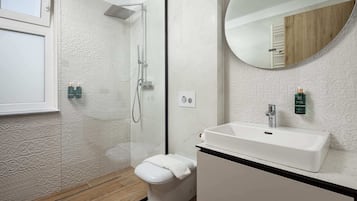 Un bagno moderno con doccia a filo pavimento, WC, lavabo e specchio.