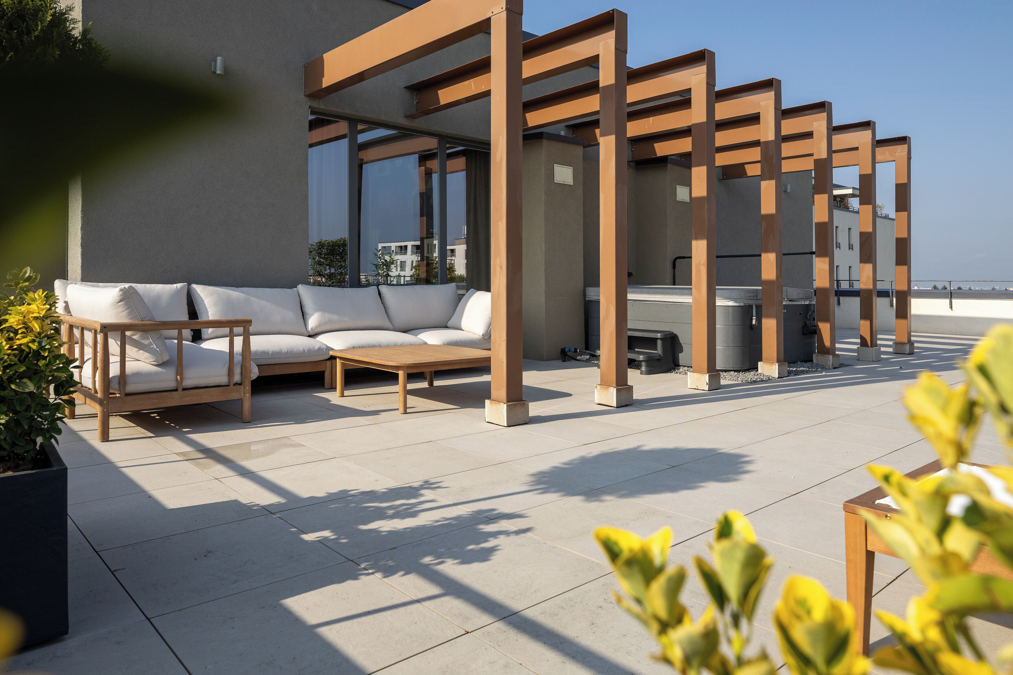 An outdoor seating area with a sofa and chairs, a pergola structure, and a view of the cityscape.