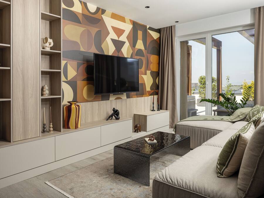 A modern living room with a flat-screen TV mounted on a geometric-patterned wall, a sofa, a coffee table, and a bookshelf with decorative items.