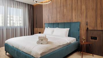 A modern hotel room with a teal bed, white linens, a wooden panel wall, and a small bedside table with a lamp.