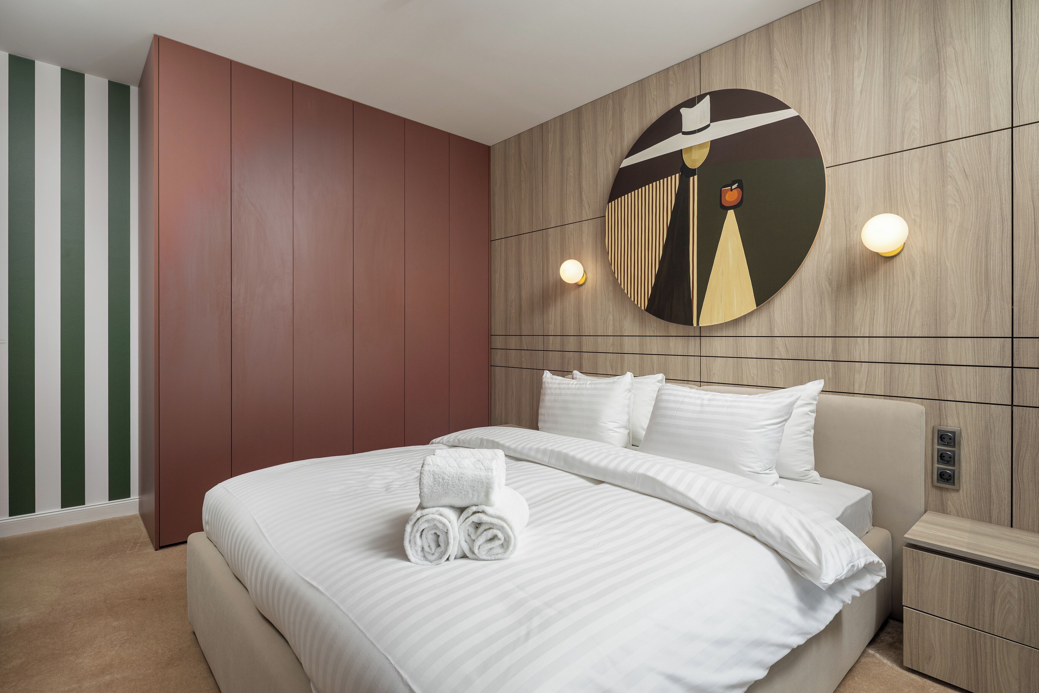 Una habitación de hotel moderna con una cama grande, un cabecero de madera y una obra de arte circular colgada en la pared.