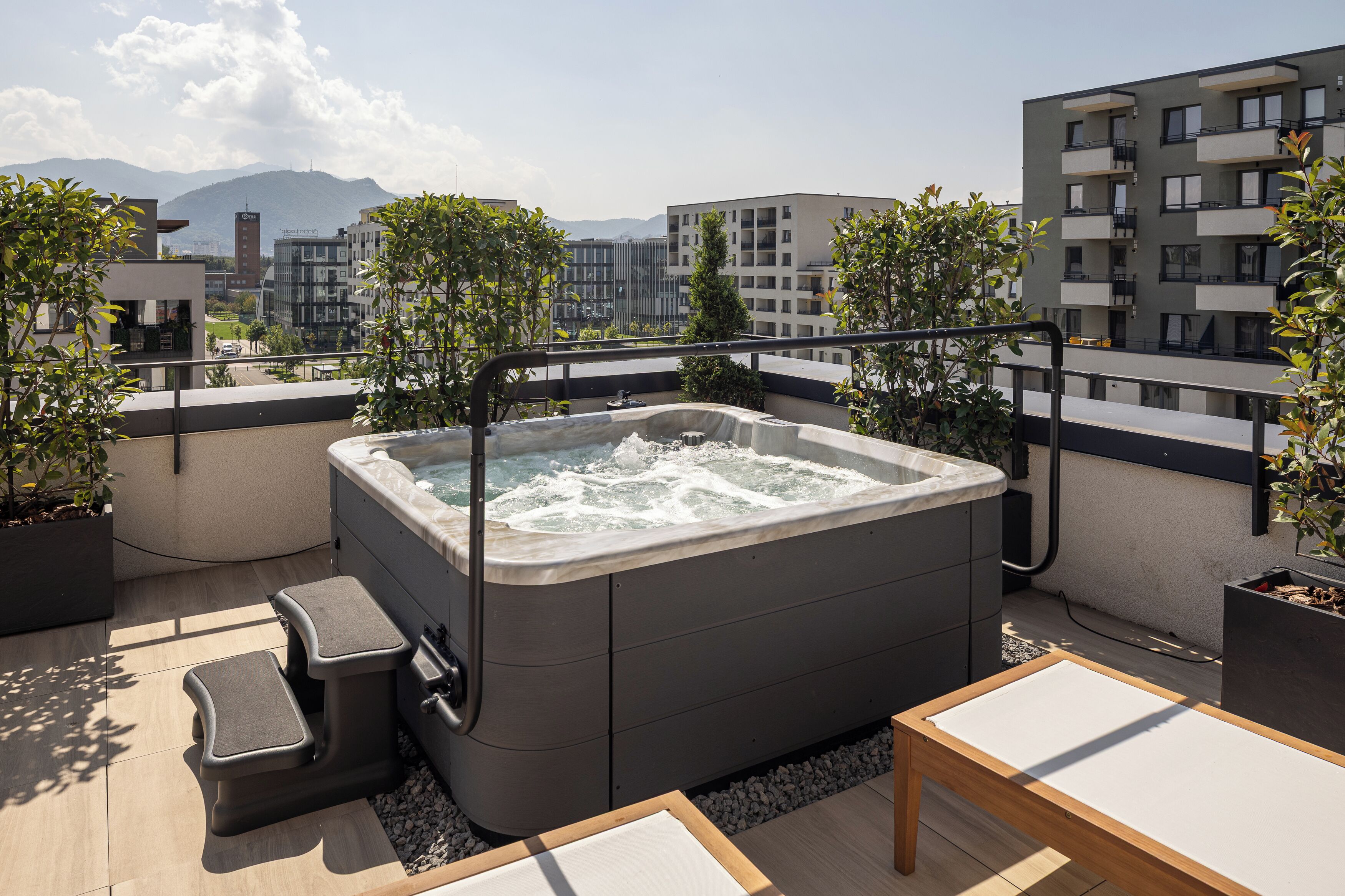 Een terras op het dak met een jacuzzi, een zithoek en potplanten.