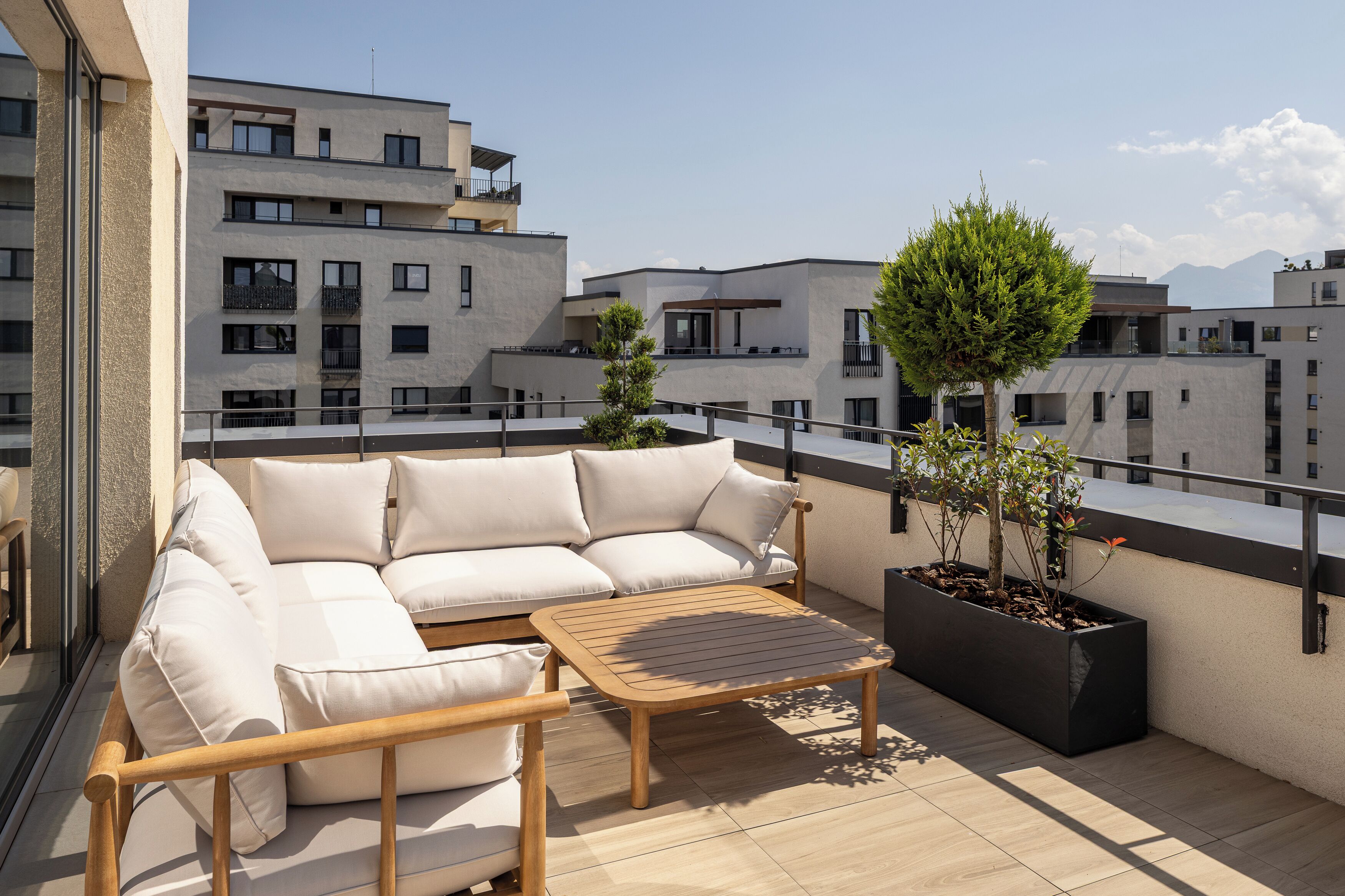 A balcony with a white sofa, wooden table, and potted plants.