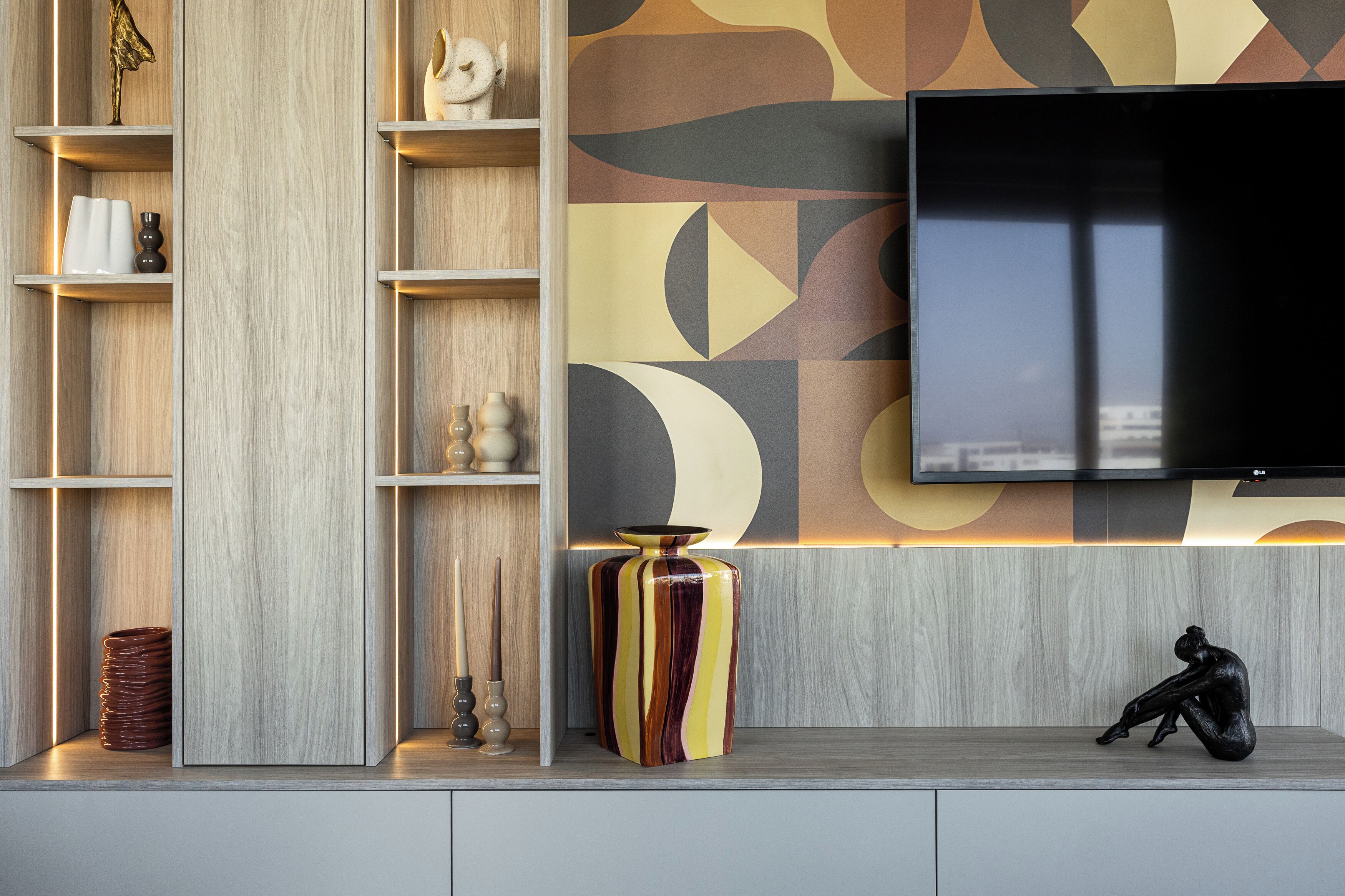 A modern living room with a flat-screen TV mounted on the wall, wooden shelving units, and decorative items.
