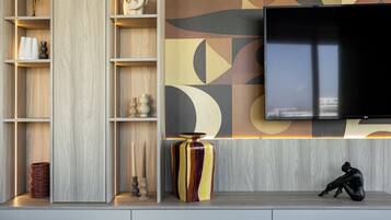 A modern living room with a flat-screen TV mounted on the wall, wooden shelving units, and decorative items.