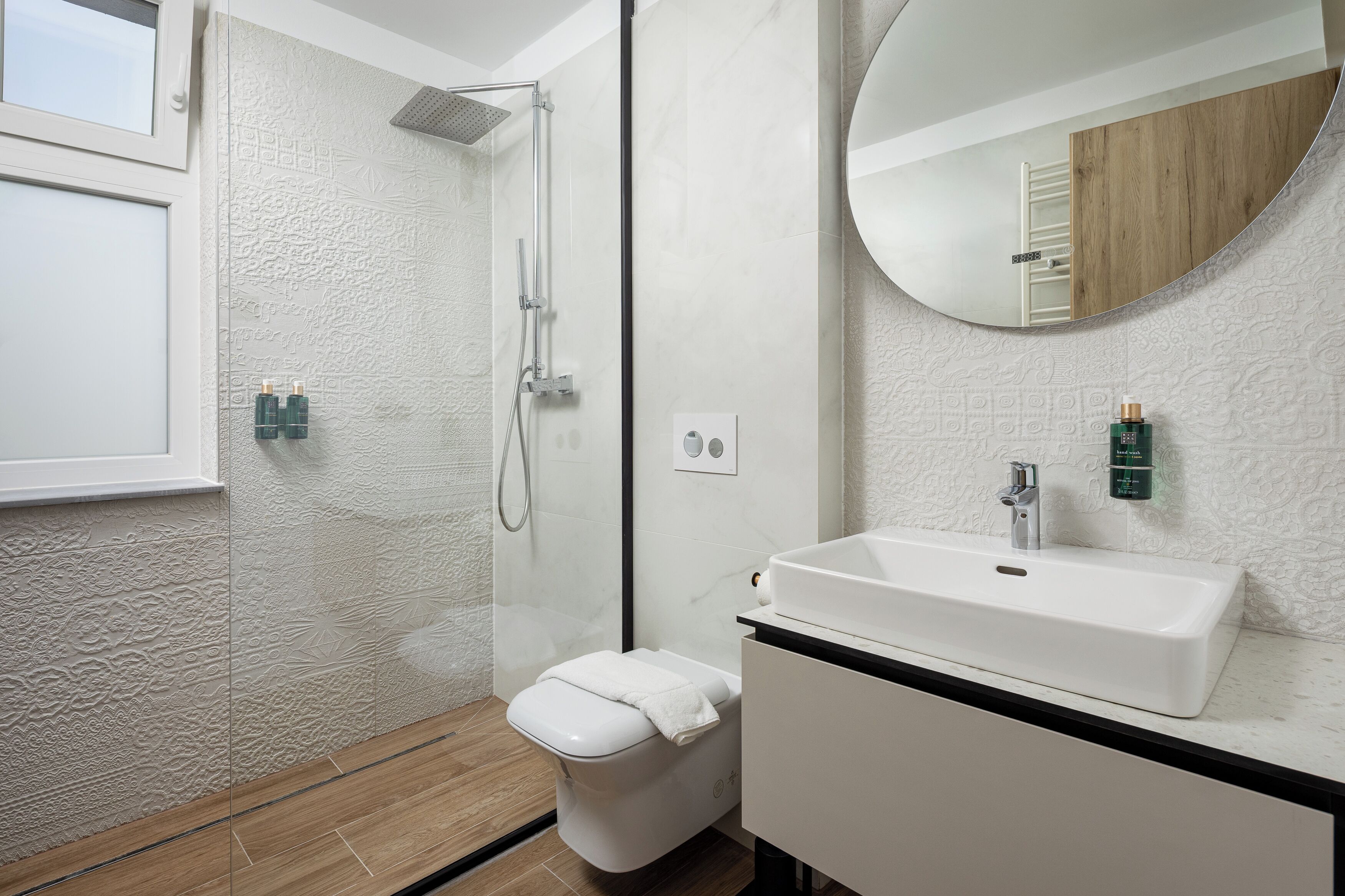 A modern bathroom with a shower, toilet, sink, and a large mirror.