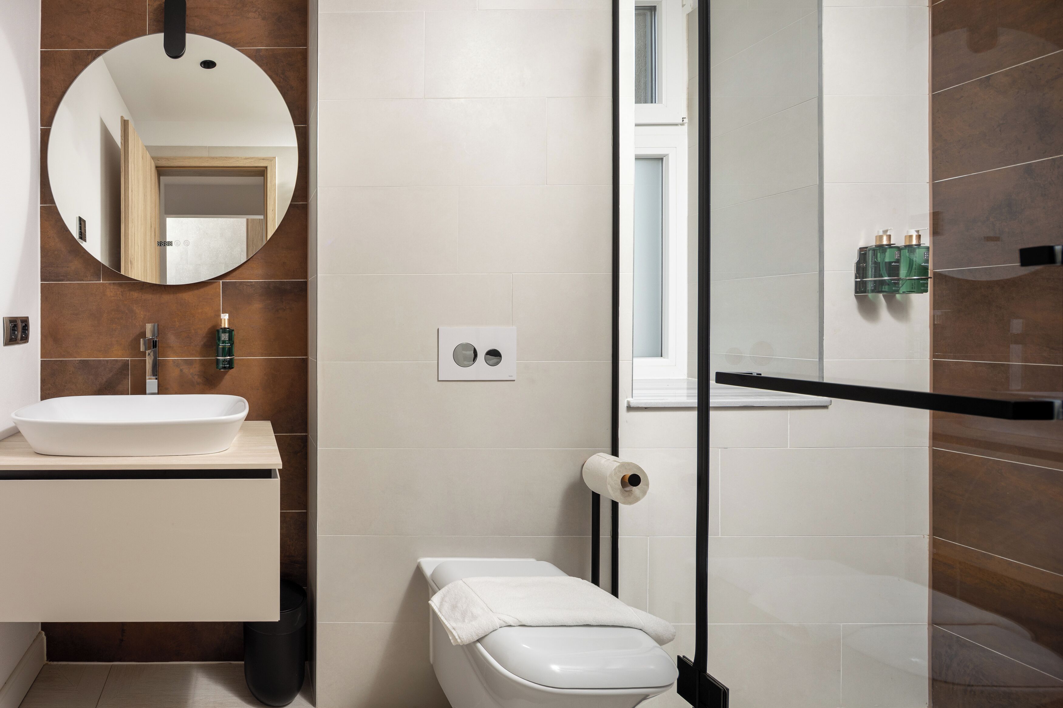 A modern bathroom with a white sink, mirror, toilet, and shower area.