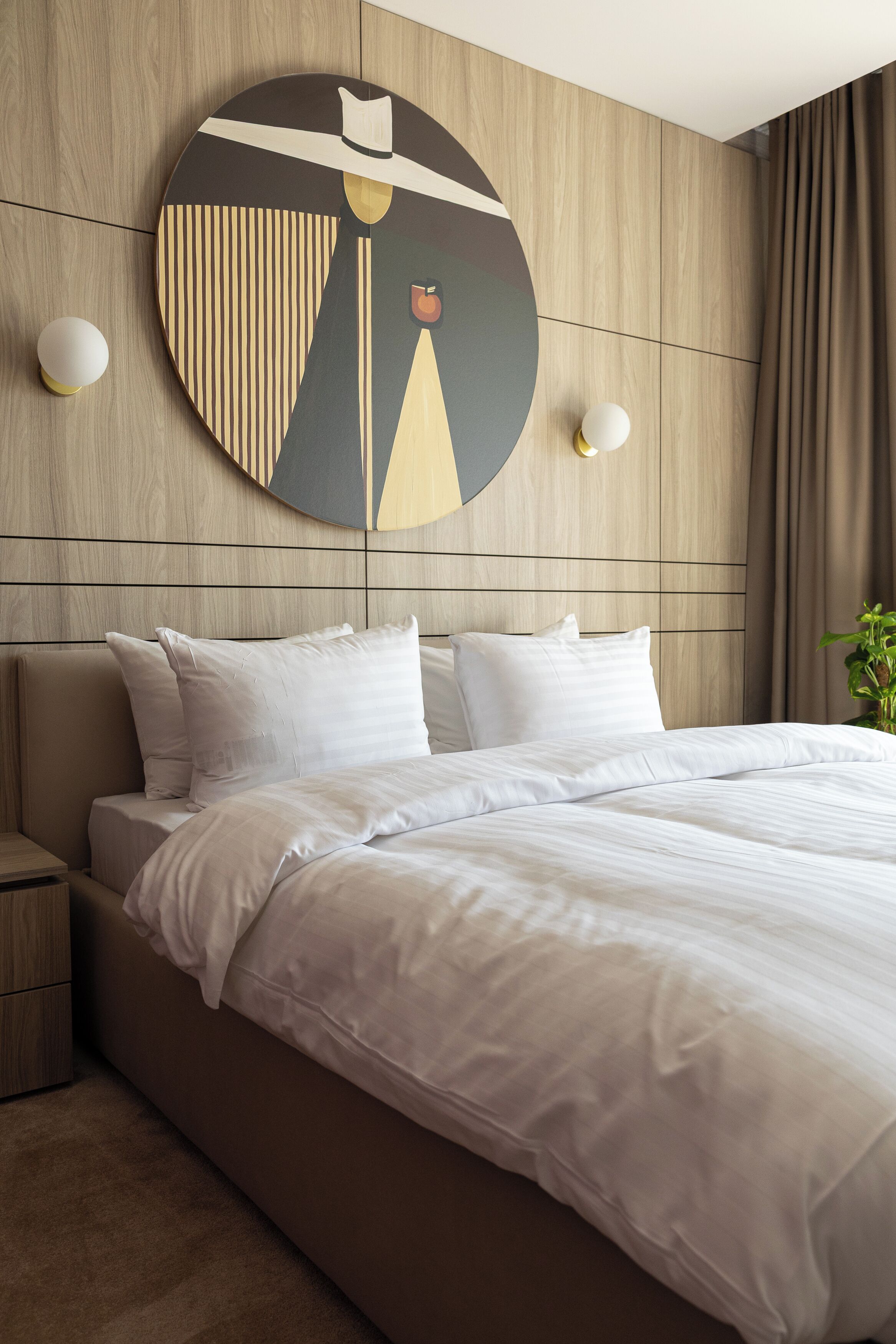 A modern hotel room with a large bed, a wooden headboard, and a wall-mounted abstract artwork.
