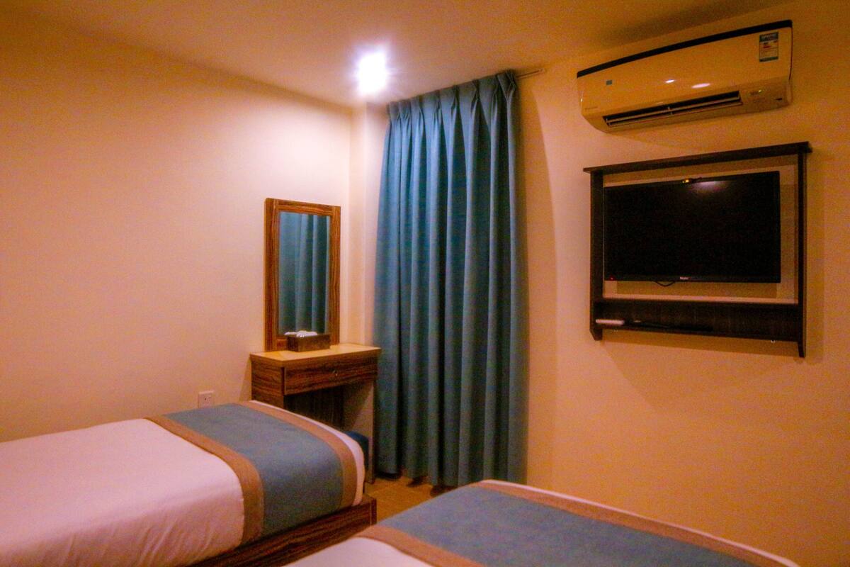 Una habitación de hotel con dos camas, televisión, aire acondicionado y espejo.