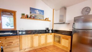 Una cucina con mobili in legno, un frigorifero in acciaio inossidabile, una finestra e un orologio appeso al muro.