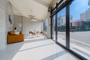 A modern living room with a sofa, chairs, and a table. Large windows provide a view of the street. - BestHome929 (Liuqiu)