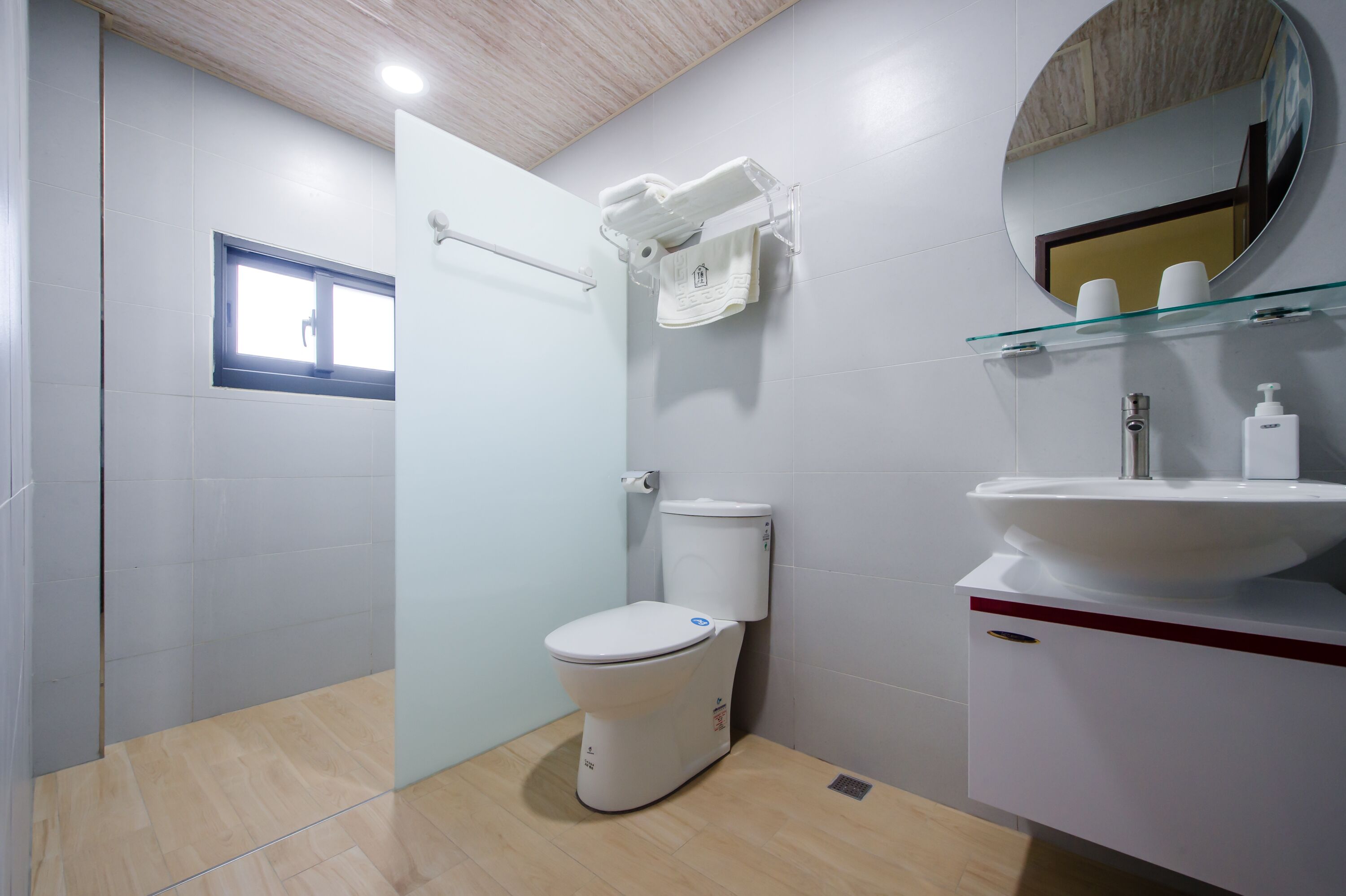 Un baño moderno con inodoro, un estante de vidrio con artículos de aseo y un espejo.