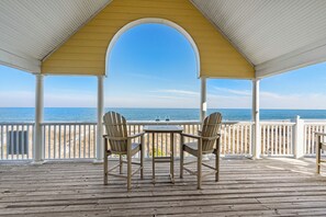 A wooden deck with two Adirondack chairs and a table, overlooking a beach with the ocean in the background. - Marlin View: Oceanfront w/ Pool, Walk to Dining (Garden City)