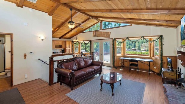 A spacious living room with a wooden ceiling, a brown leather sofa, a coffee table, and a view of the outdoors through large windows. - Monterey Mtn View Cabin  Views Moonridge (Big Bear Lake)