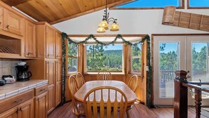 A wooden interior with a dining table and chairs, a coffee maker, and a view of the outdoors through large windows. - Monterey Mtn View Cabin  Views Moonridge (Big Bear Lake)