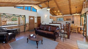A spacious living room with a leather sofa, wooden coffee table, and a dining area with a wooden table and chairs. - Monterey Mtn View Cabin  Views Moonridge (Big Bear Lake)