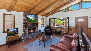 A cozy living room with a fireplace, leather sofa, and a television. - Monterey Mtn View Cabin  Views Moonridge (Big Bear Lake)