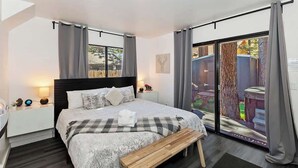 Un dormitorio moderno con una cama grande, un banco de madera, una mesita de noche y vistas al exterior a través de una puerta corrediza de vidrio.