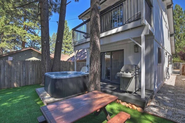 Una casa de dos pisos con jacuzzi, parrilla y mesa de picnic en el patio trasero.