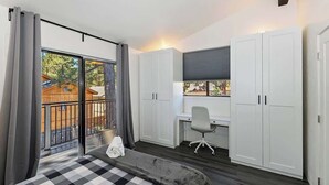 Un dormitorio con una cama grande, un escritorio y una silla. Hay una puerta corrediza de vidrio que da a un área exterior.