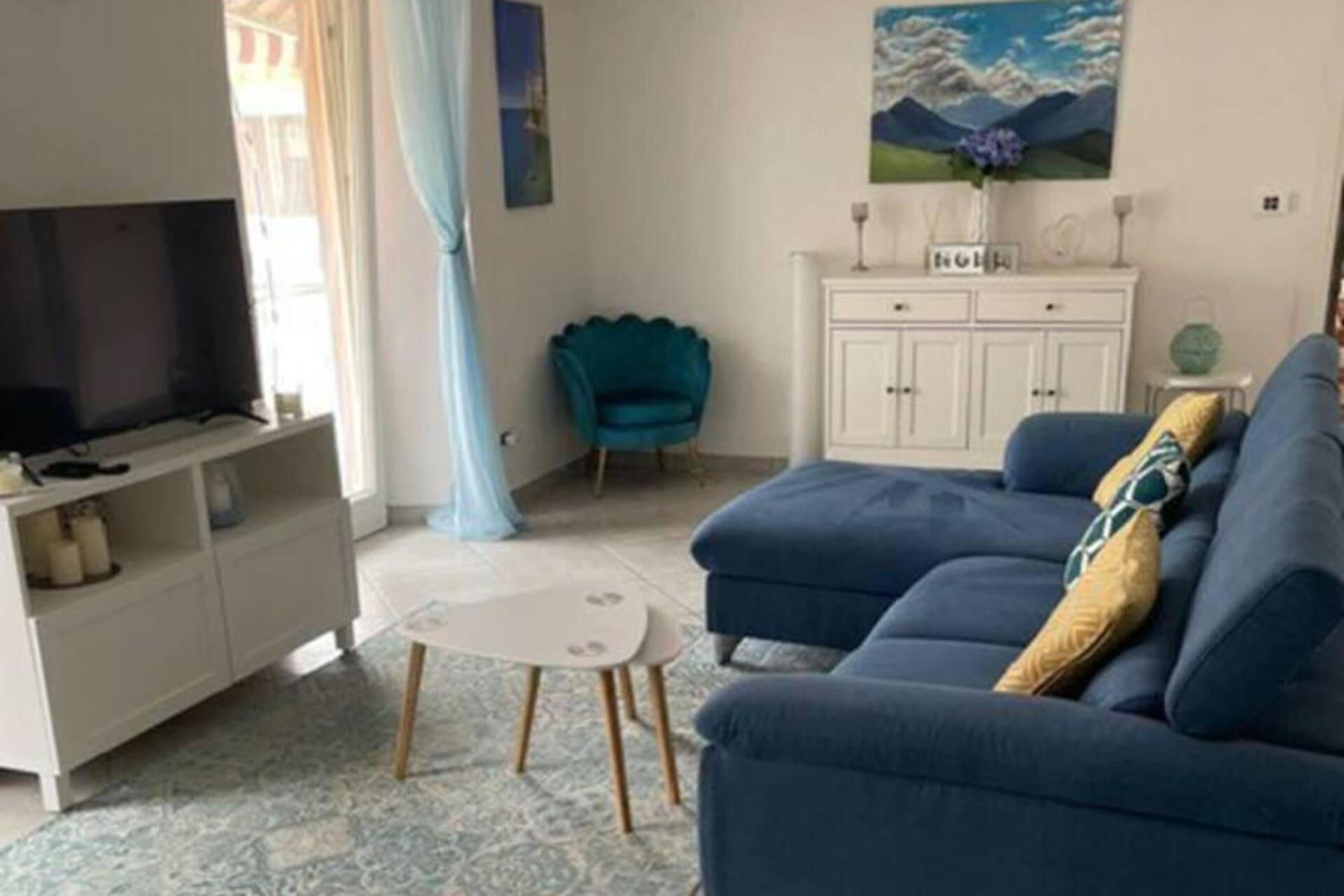 A living room with a sofa, a television, a cabinet, and a painting on the wall.