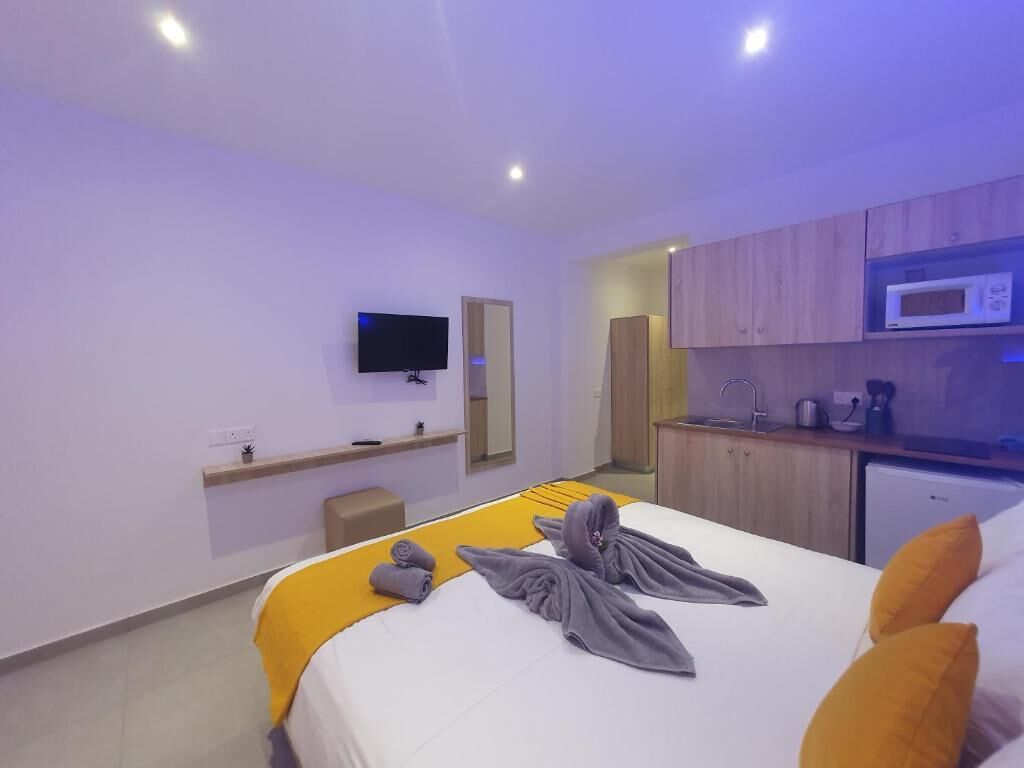 A modern hotel room with a bed, a television, a microwave, and a small kitchenette.