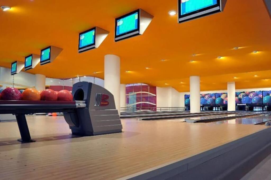 A bowling alley with multiple lanes, a bowling ball rack, and overhead monitors.